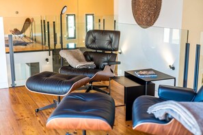 A modern room with a glass partition, leather seating, a small table, and a hanging light fixture.