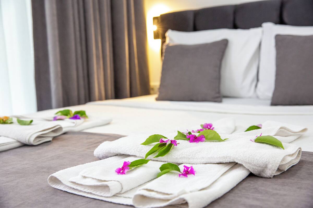 Een net opgemaakt bed met witte lakens, decoratieve bloemen, een hoofdbord en een gordijn in een hotelkamer.