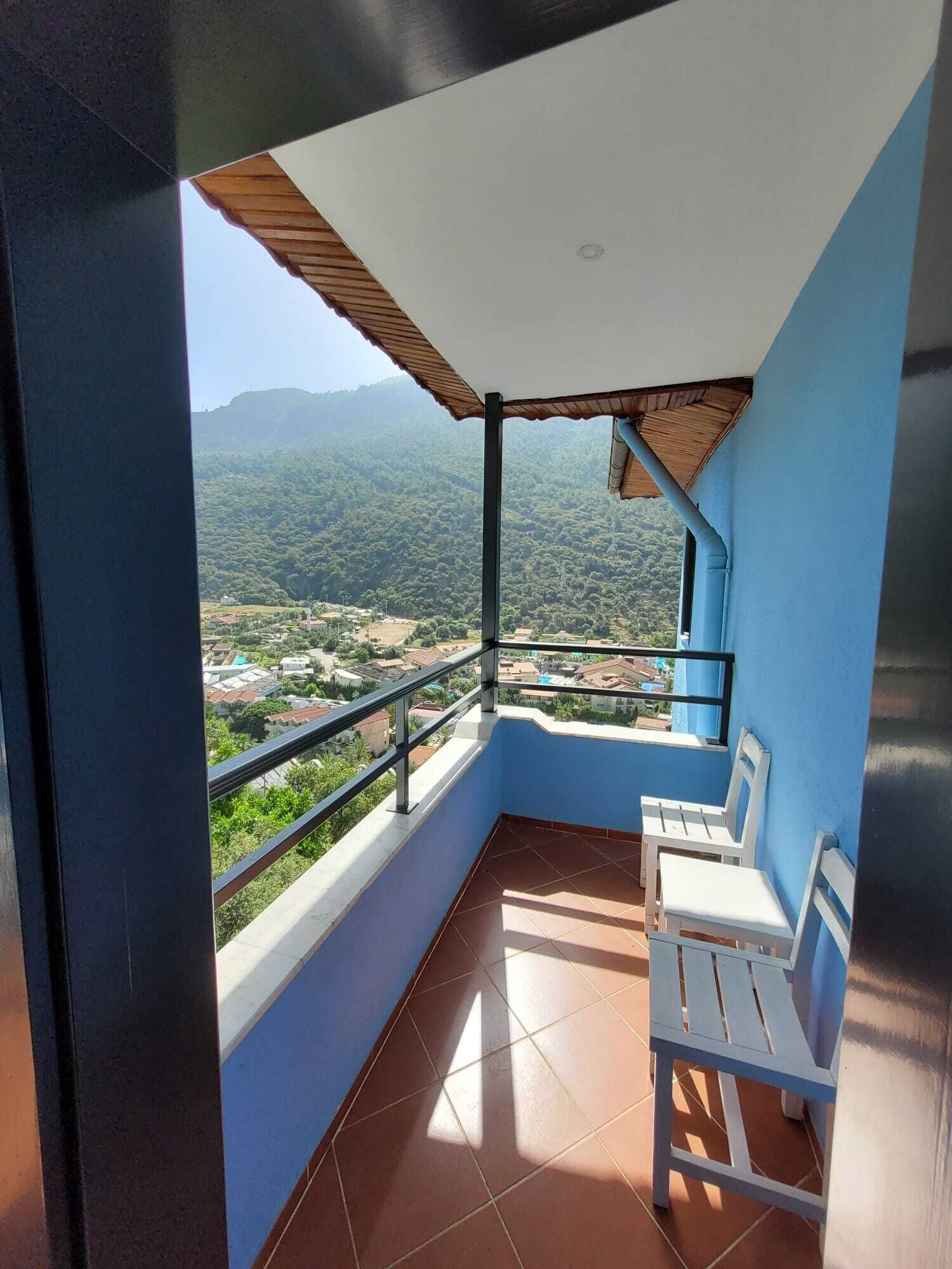 A balcony with a view of a mountainous landscape, a tiled floor, and two white chairs.