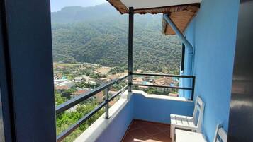 A balcony with a view of a mountainous landscape, a tiled floor, and two white chairs.