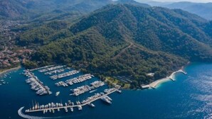 Eine Vogelperspektive einer Marina, umgeben von Hügeln, mit vor Anker liegenden Booten und freiem Blick auf die Küste.