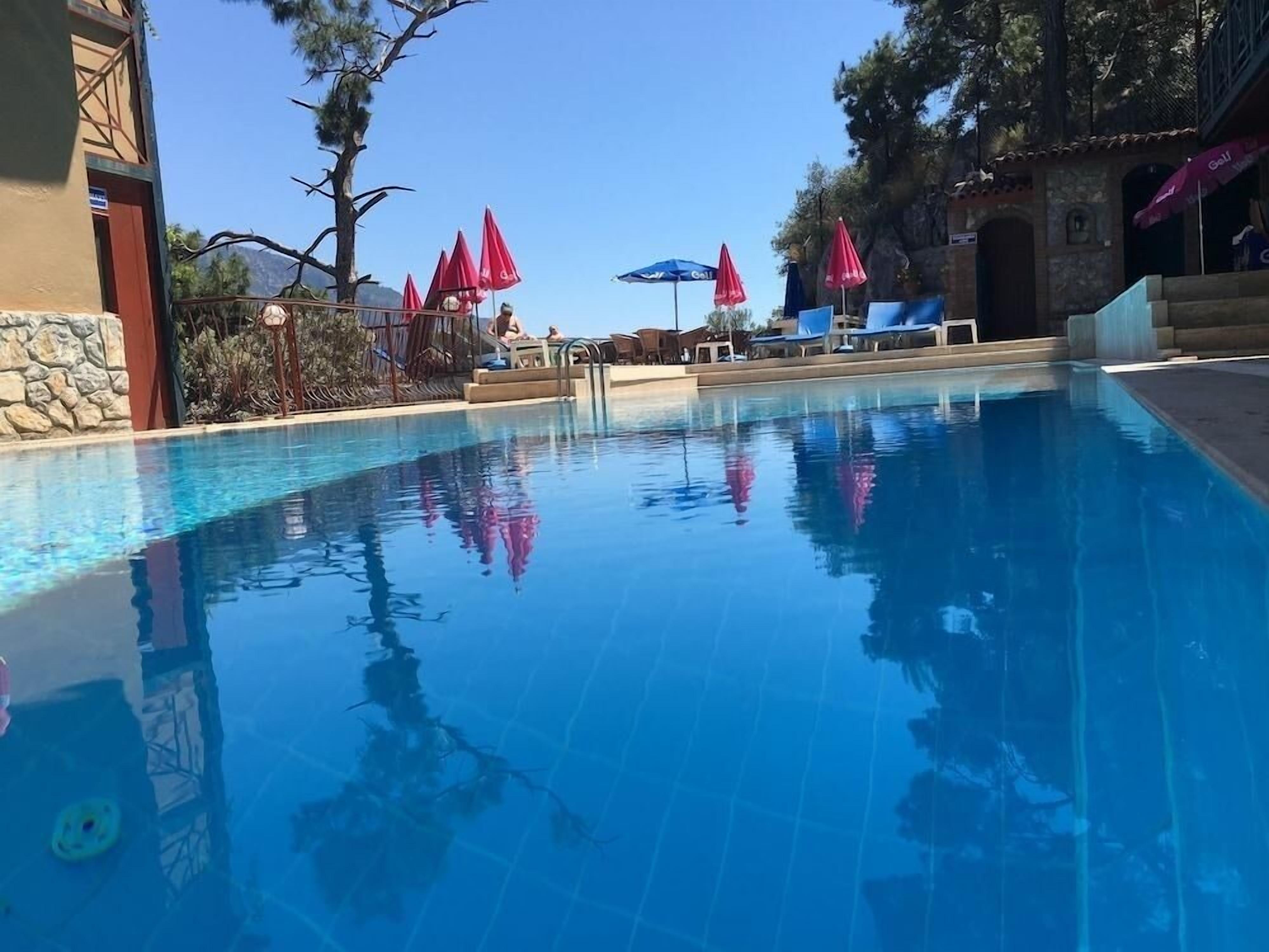 Una piscina cristalina con sillones de descanso y sombrillas, rodeada de muros de piedra y árboles.