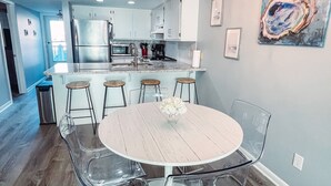 Une cuisine moderne avec des meubles blancs, un réfrigérateur en acier inoxydable et un coin repas comprenant une table ronde et des chaises.