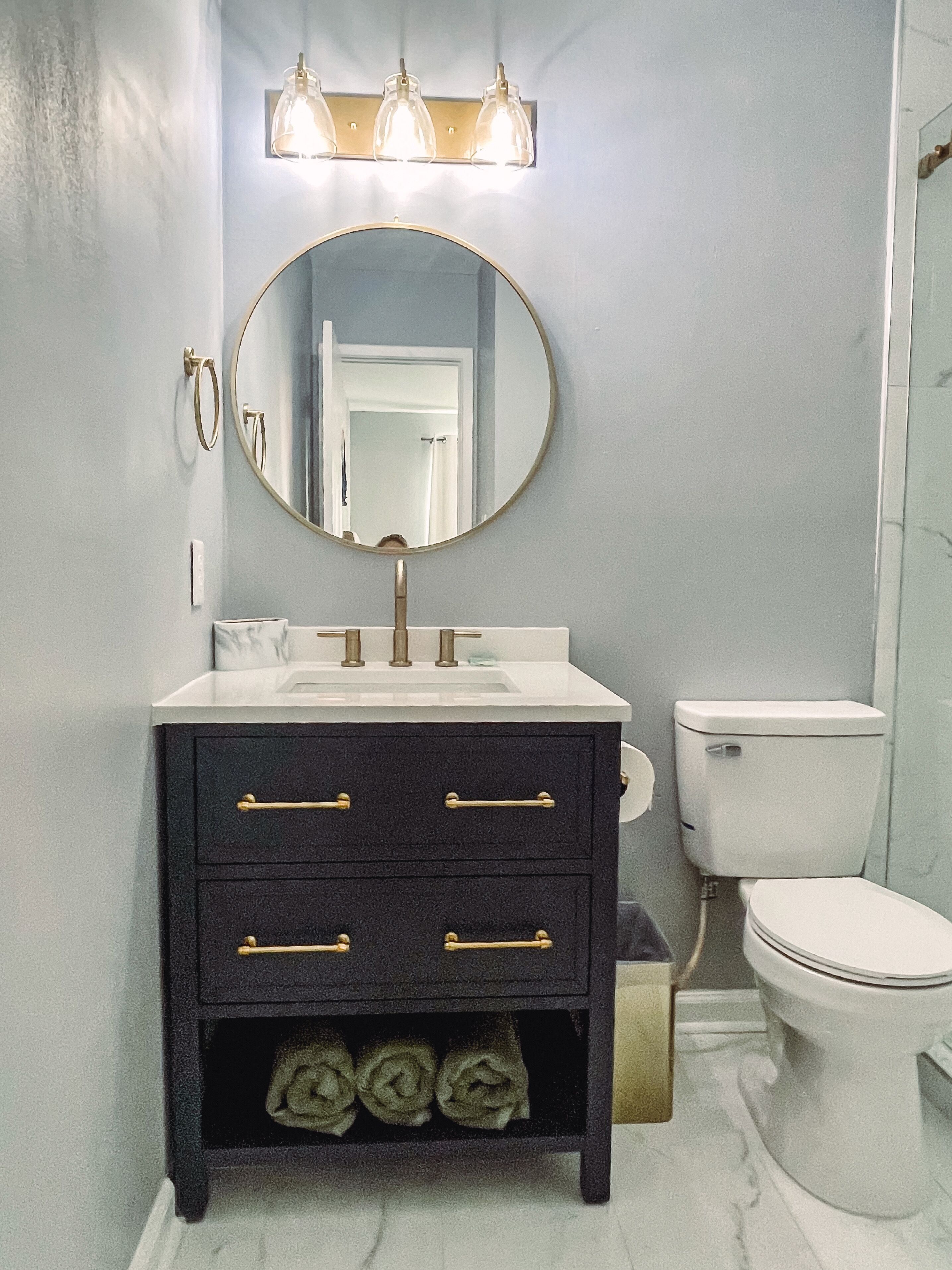 A bathroom with a round mirror, a sink, and a toilet.