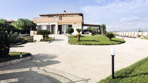 A modern two-story house with a driveway leading to the entrance, surrounded by well-maintained lawns and small trees. - Isula Relax - Villa with pool (Modica)