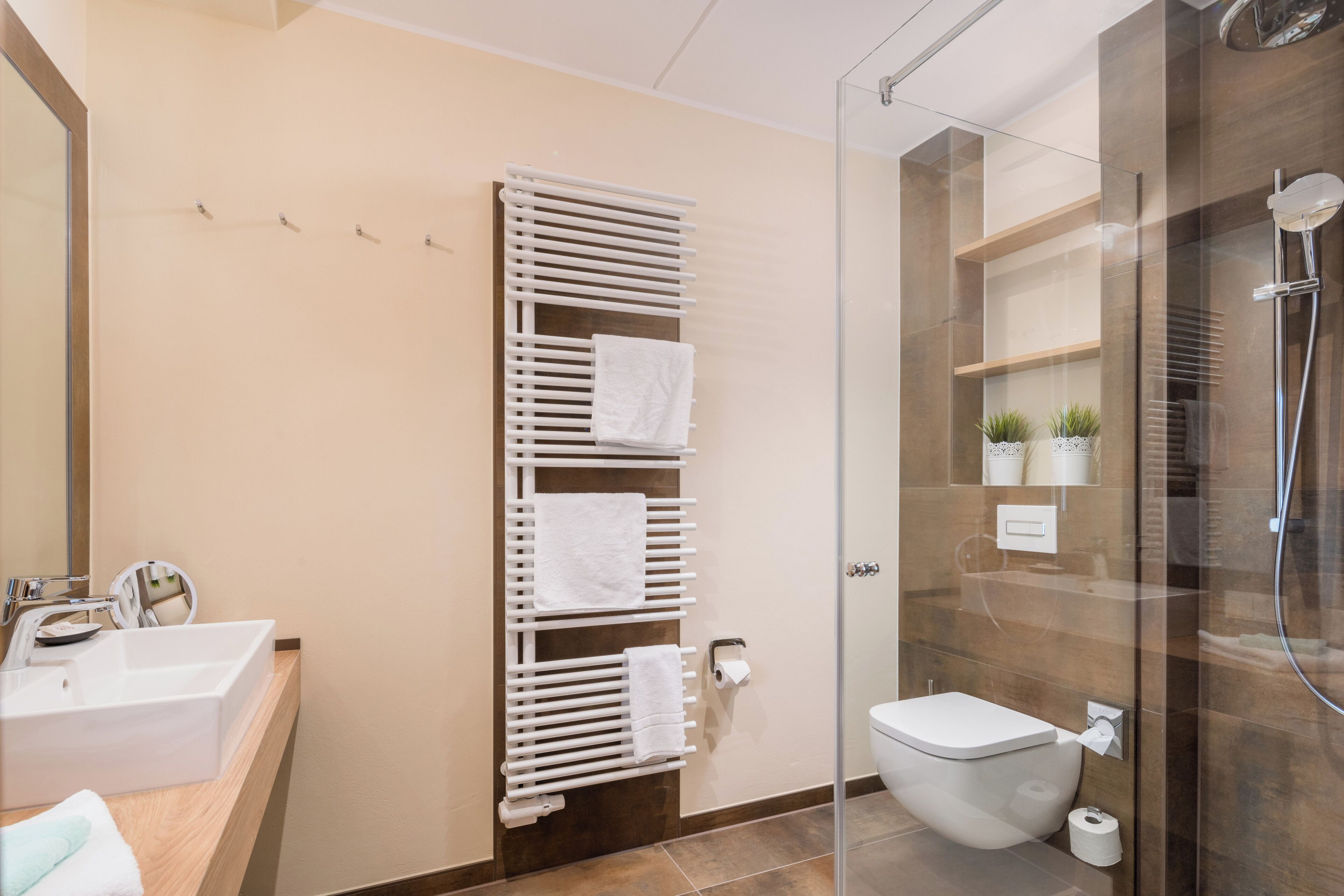 A modern bathroom with a glass shower enclosure, a white sink, and a towel rack with multiple towels.