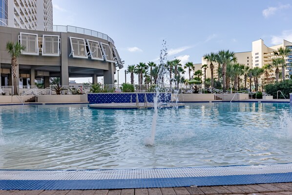 Relax by the pool surrounded by a tranquil water feature and lush palm trees.