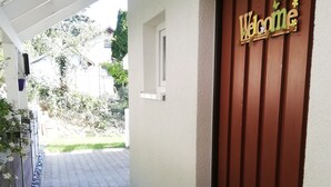 A pathway leading to a door with a 'Welcome' sign, a small window, and a wall-mounted light fixture.