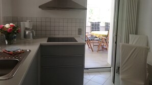 A kitchen with a modern stove, a coffee maker, and a sink. There is a dining area with a table and chairs visible through an open door.