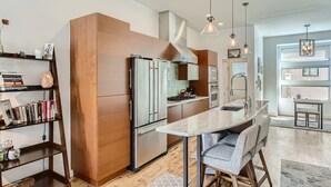 A modern kitchen with stainless steel appliances, a wooden accent wall, and a central island with bar stools. - Beautiful, Modern Pet-Friendly Downtown Executive Rental (Denver)