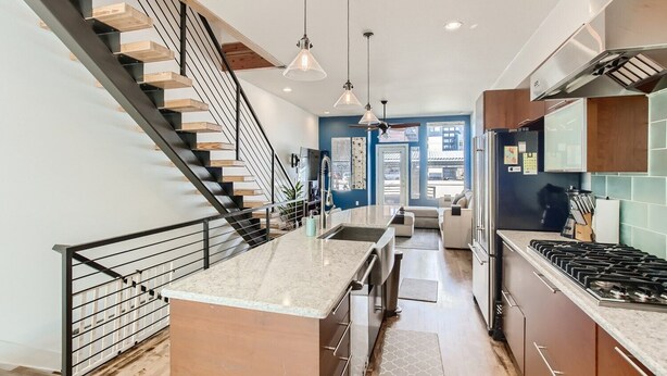 A modern kitchen with a central island, stainless steel appliances, and a staircase with wooden steps. - Beautiful, Modern Pet-Friendly Downtown Executive Rental (Denver)