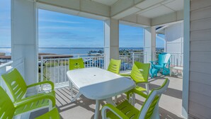 A covered outdoor seating area with a white table and green chairs, overlooking a beach and ocean. - Book Sandtastic Penthouse 421A | Sandbridge Vacation Rental (Virginia Beach)