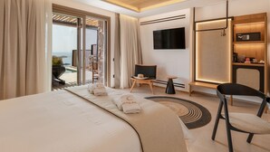 A modern hotel room with a large bed, a TV, a seating area with a chair and a small table, and a view of the outdoors. - Calma Suites Mykonos (Mykonos)