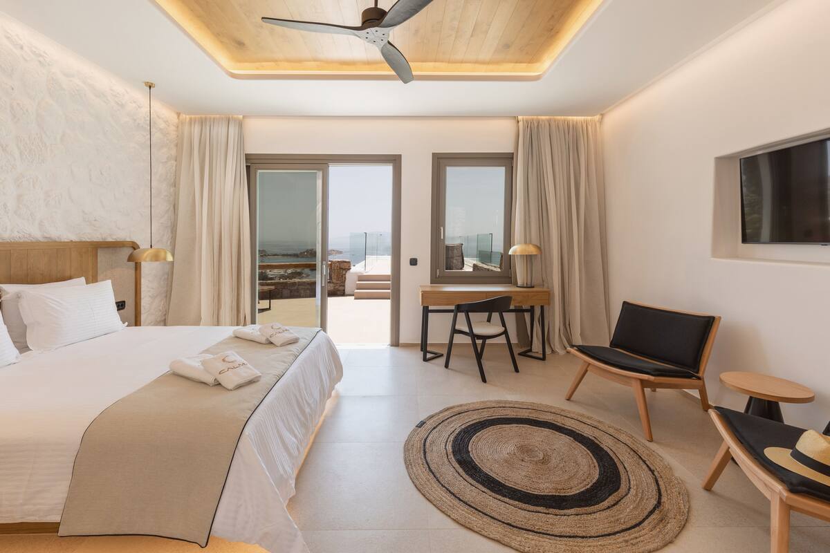 A modern hotel room with a large bed, a desk, a chair, and a small table.