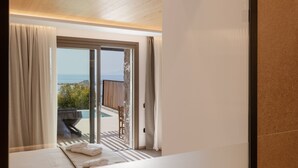 A modern hotel room with a large sliding glass door leading to an outdoor area with a barbecue and seating. - Calma Suites Mykonos (Mykonos)
