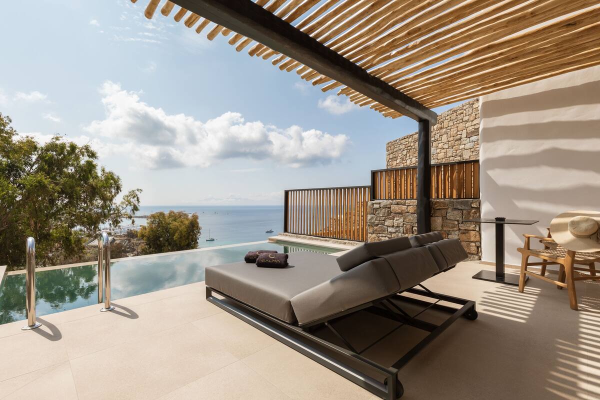 A modern outdoor lounge area with a pool, a stone wall, and a view of the sea.