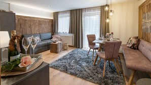 A modern living room with a sofa, dining table, and chairs. There is a fireplace, a coffee table, and a rug. - Landhaus Dengg in Gerlos: Rosengarten Apartment for 2 to 4 people (Gerlos)