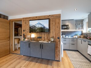 Een moderne keuken met houten kasten, een grote flatscreen televisie boven de aanrecht en een wand met houten lijst.