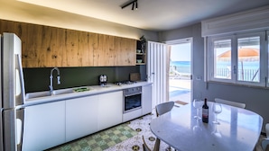 Eine moderne Küche mit weißen Schränken, einer Wand in Holzoptik, einem Spülbecken und einem Backofen. Ein Esstisch ist mit zwei Weingläsern und einer Weinflasche gedeckt.
