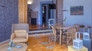 Ein modernes Wohnzimmer mit einer Couch, einem Esstisch und Stühlen. Ein Fernseher ist an der Wand befestigt und über dem Tisch hängt ein Gemälde.