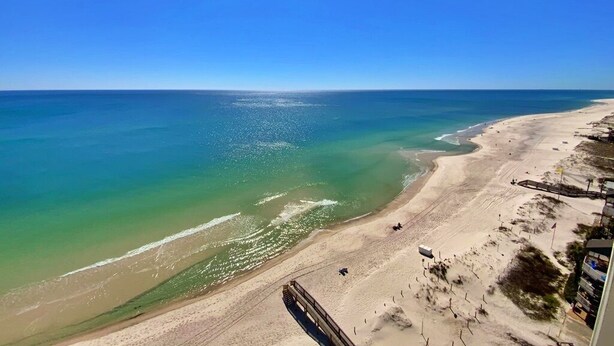 A beach with a wooden boardwalk, clear blue sky, and calm sea. - Beachfront, Pool & Sunroom (Gulf Shores)