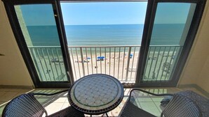 A balcony with a view of the beach, a round table, and two chairs. - Beachfront, Pool & Sunroom (Gulf Shores)