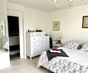 Ein Schlafzimmer mit Bett, Kommode, Nachttisch und Fenster.