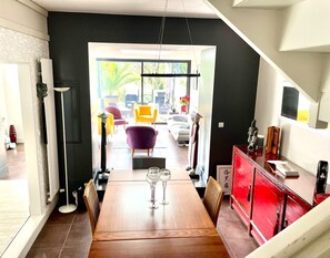 Ein Essbereich mit Holztisch, Stühlen und Weingläsern. Rechts befindet sich ein roter Schrank und eine Statue. Der Raum hat eine schwarze Wand und Blick ins Freie.