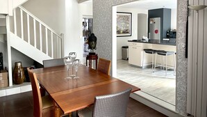 A modern dining area with a wooden table and chairs, a staircase, and a kitchen visible through an open doorway.