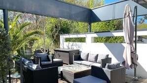 An outdoor patio with wicker furniture, a glass table, and a covered seating area.