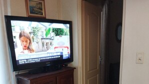 A living room with a television on a wooden cabinet, a grey sofa, and a door leading to another room. - Village house 20 minutes from the beach (Piedicroce)