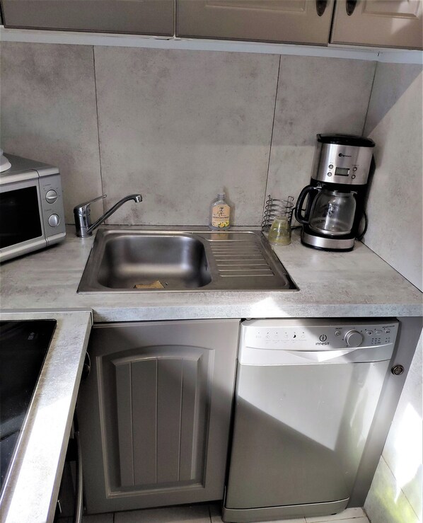 Een compacte keuken met een roestvrijstalen spoelbak, een koffiezetapparaat, een magnetron en een vaatwasser.