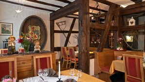 A rustic dining area with wooden beams, a wooden bench, and a table set for two with wine glasses and a candle. - Hotel-Restaurant Zum Karpfen (Obernburg)