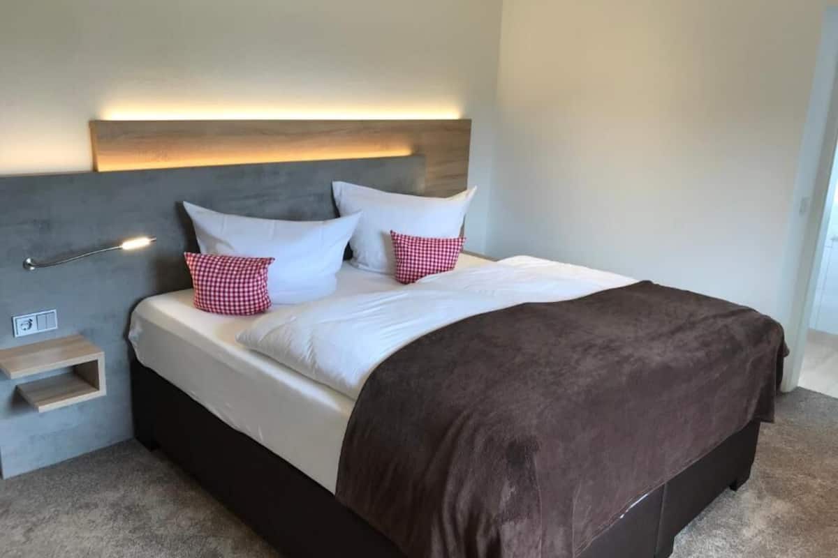 Un dormitorio moderno con cama, mesitas de noche y cabecera con iluminación integrada.