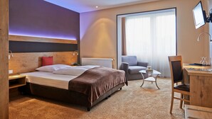 A hotel room with a large bed, a desk, a chair, a small table, and a TV mounted on the wall. - Hotel-Restaurant Zum Karpfen (Obernburg)