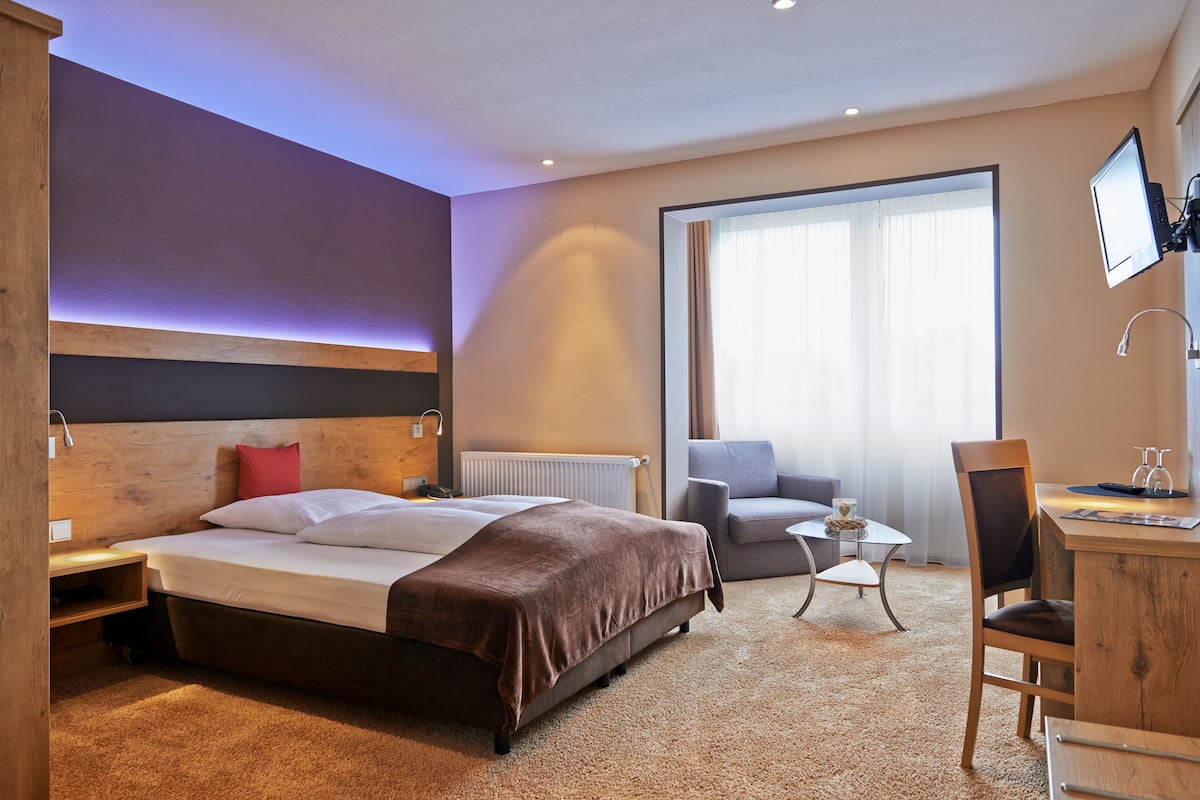Habitación de hotel con una cama grande, un escritorio, una silla, una mesita y un televisor montado en la pared.