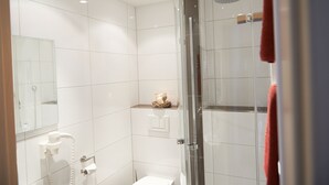 A modern bathroom with white tiles, a glass shower enclosure, a white toilet, and a towel rack. - Hotel-Restaurant Zum Karpfen (Obernburg)