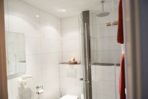 Um banheiro moderno com azulejos brancos, box de vidro, vaso sanitário branco e porta-toalhas.