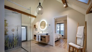 A modern bathroom with a glass shower enclosure, a wooden vanity, a round mirror, and a wooden bench with towels. - Büchelbergerei Chaletdorf (Gunzenhausen)