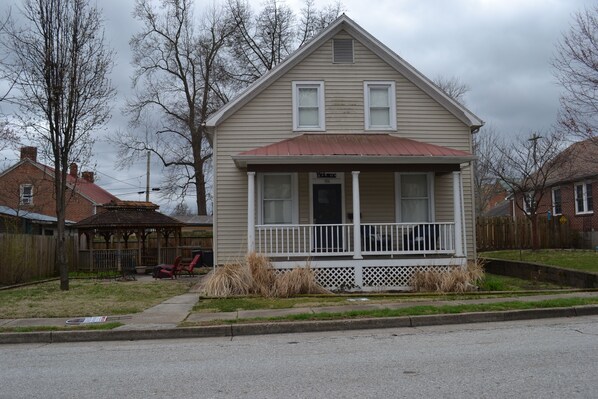 A two-story house with a front porch, a small garage, and a wooden fence.