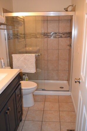 A bathroom with a glass-enclosed shower, a toilet, and a sink with a towel hanging on the wall.