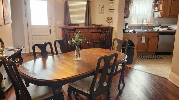 A dining area with a wooden table and chairs, a chandelier, and a kitchen in the background. - 5 bed 2 Bath in Downtown Hermann, MO (Hermann)