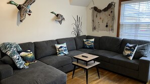 A modern living room with a grey sectional sofa, a coffee table, and decorative wall art including two mounted bird sculptures. - House minutes from Pymatuning Lake! (Jamestown)