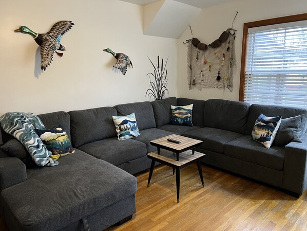 A modern living room with a grey sectional sofa, a coffee table, and decorative wall art including two mounted bird sculptures. - House minutes from Pymatuning Lake! (Jamestown)