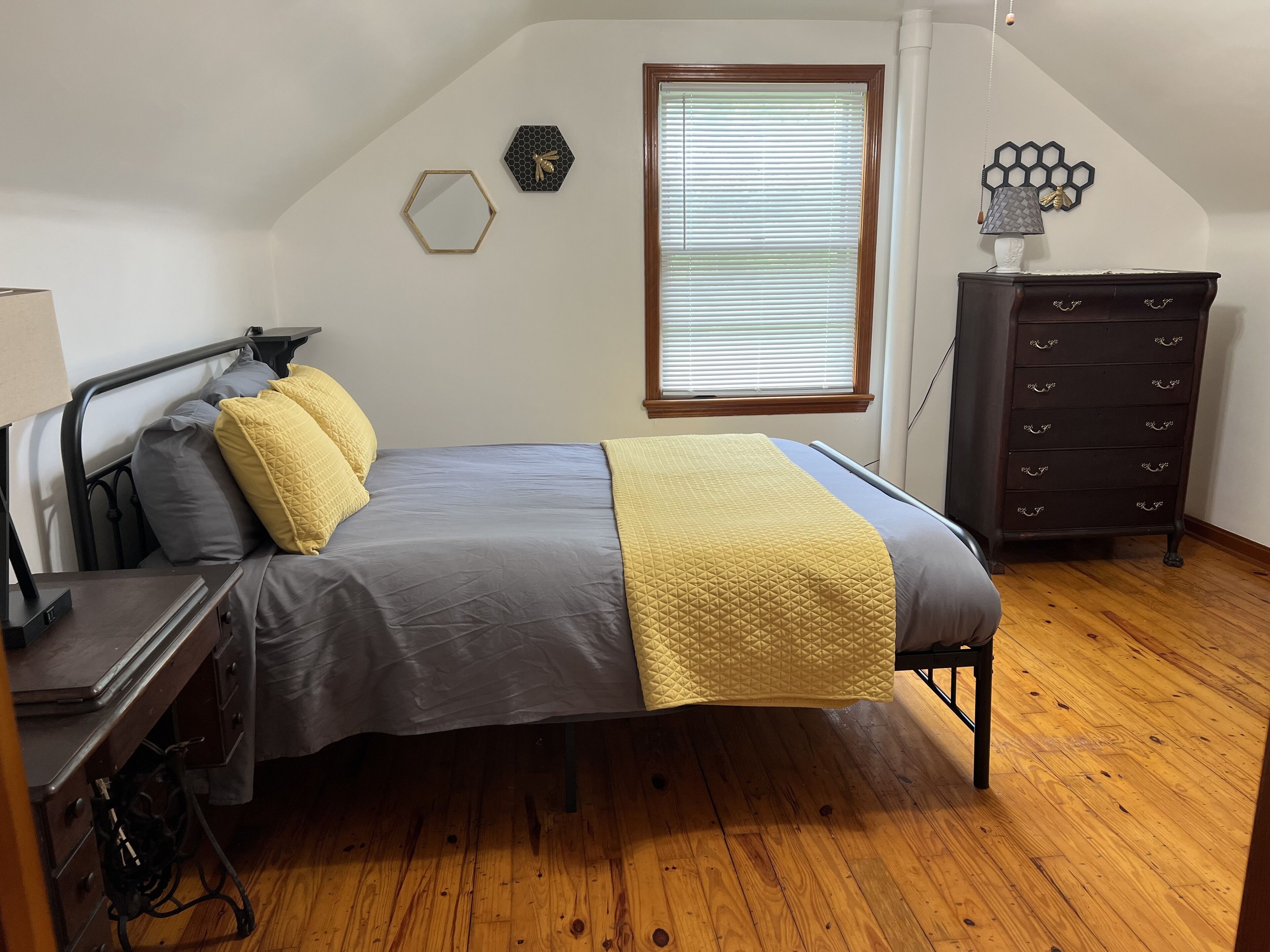 Un dormitorio con cama, cómoda, ventana con persianas y un adorno en la pared.