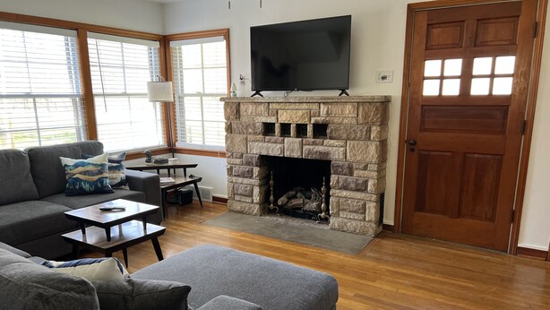 A living room with a stone fireplace, a large flat-screen TV, a sofa, and a dining area. - House minutes from Pymatuning Lake! (Jamestown)