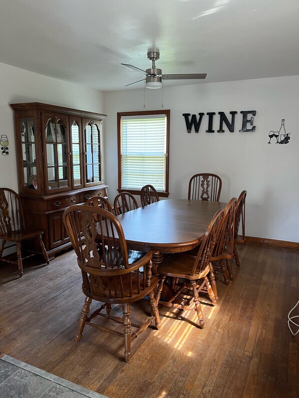 A dining room with a wooden table and chairs, a wooden cabinet, a ceiling fan, and a window with blinds.