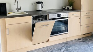 Una cocina moderna con armarios de madera, horno empotrado, lavavajillas y cafetera.