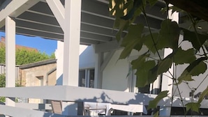 Un espacio exterior techado con un banco de hormigón, una mesita y césped artificial verde.