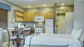 A compact hotel room with a bed, a small kitchenette, a dining area with a table and chairs, and a bathroom with a toilet and sink.